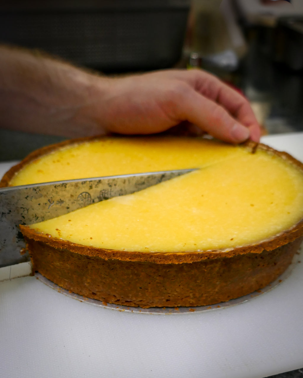 Person cutting a lemon tart with a knife on a white surface